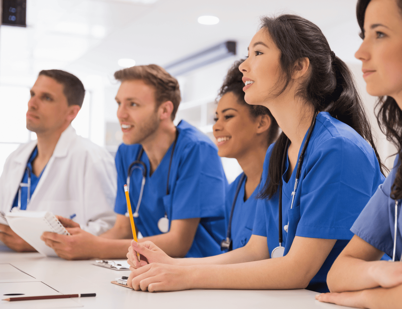 Group of medical students in blue scrubs engaged in hands-on learning in a classroom setting.